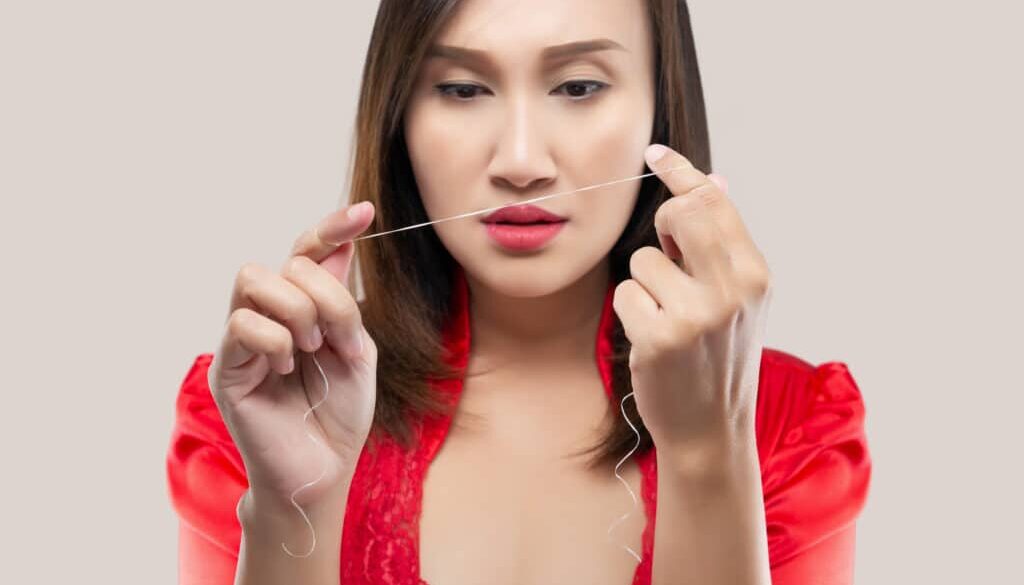 Asian woman in red silk robe cleaning teeth with dental floss on